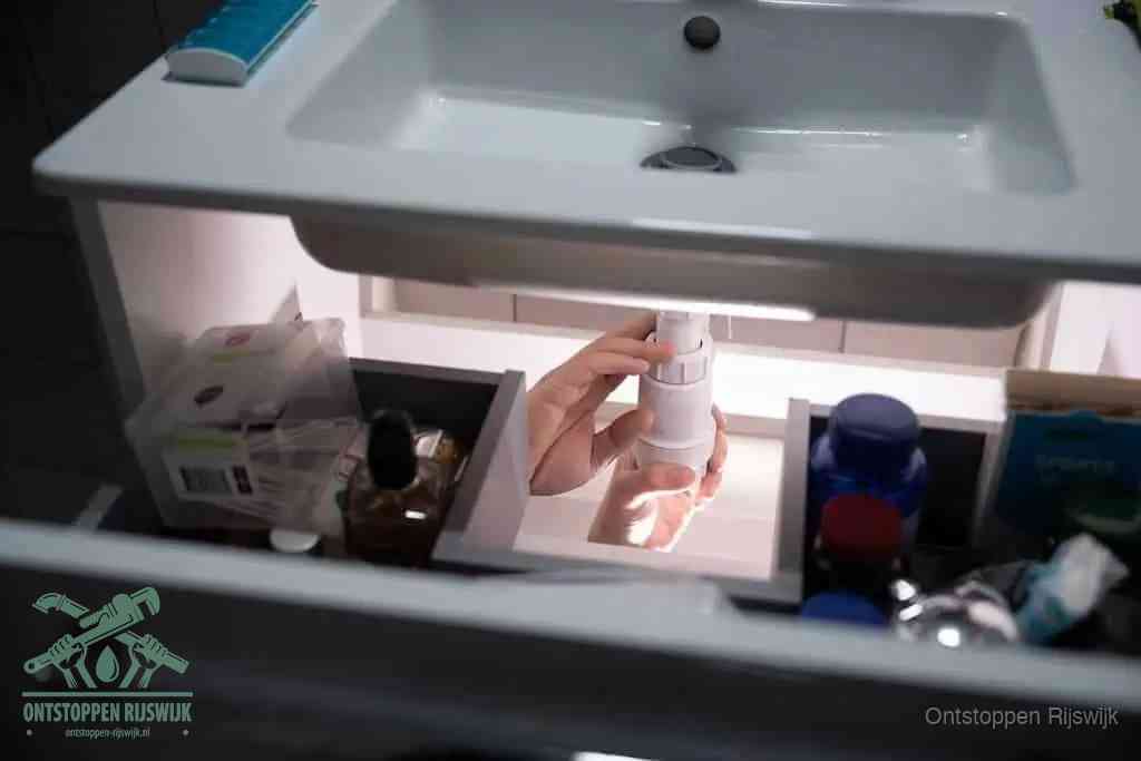 Een pompfles met zeep boven een wastafel, de heet water en afwasmiddel-methode om een vetprop in de afvoer los te maken in Rijswijk