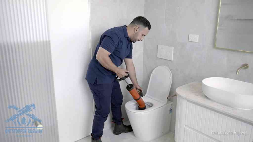 Een monteur buigt over een wandcloset en duwt met de hand een persluchtontstopper in de toiletpot om de verstopping handmatig los te maken in Rijswijk