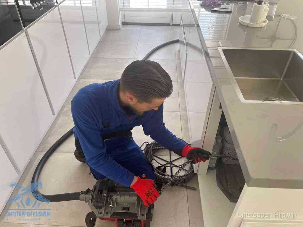 Een monteur ontstopt de keukenafvoer onder de spoelbak met een elektrische veermachine in Rijswijk