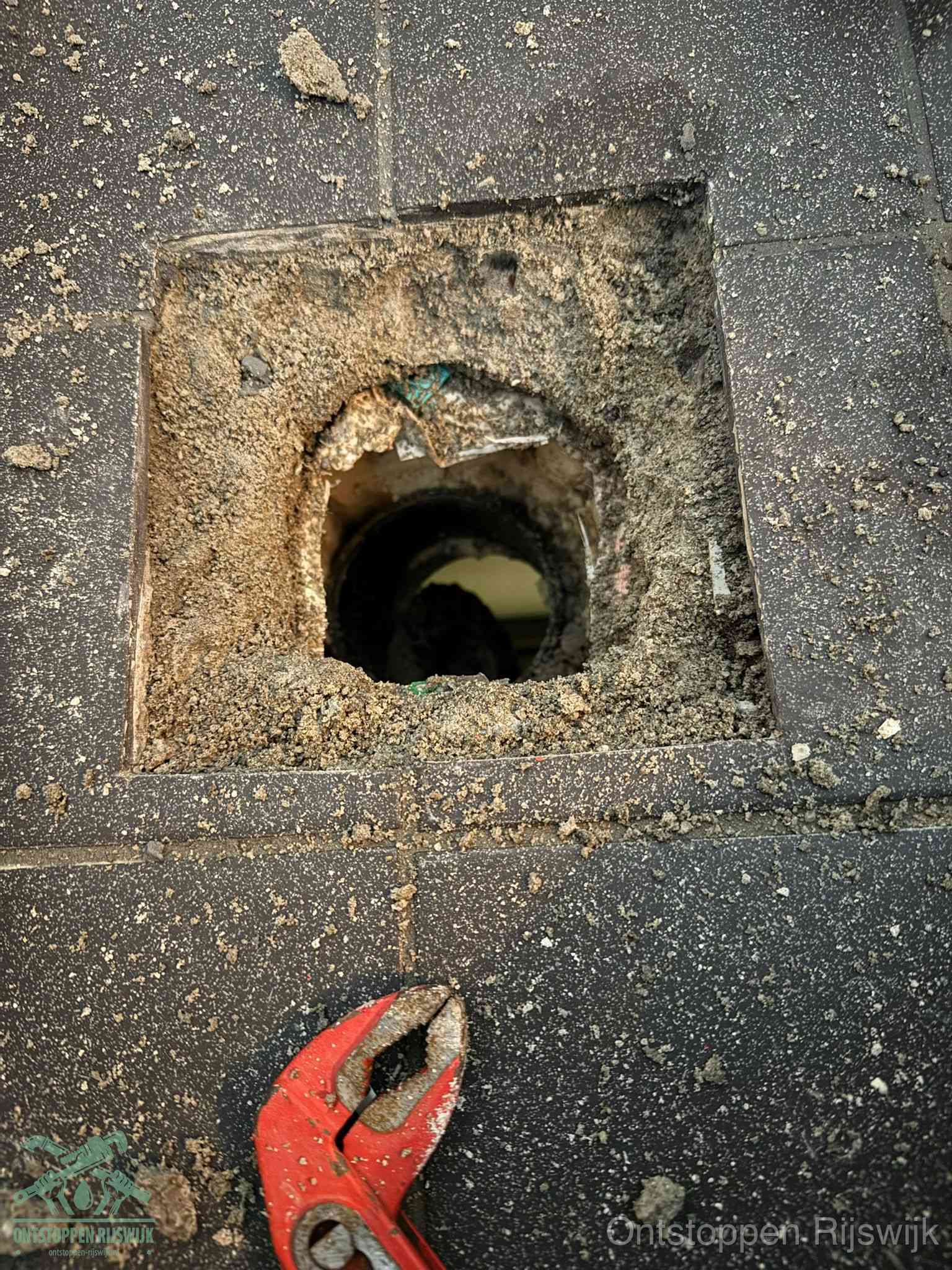 Een geopend rioolputje in een betontegelvloer met losgemaakt rooster en een zichtbare ronde afvoerbuis, het achterhalen waar de afvoerverstopping zit in Rijswijk