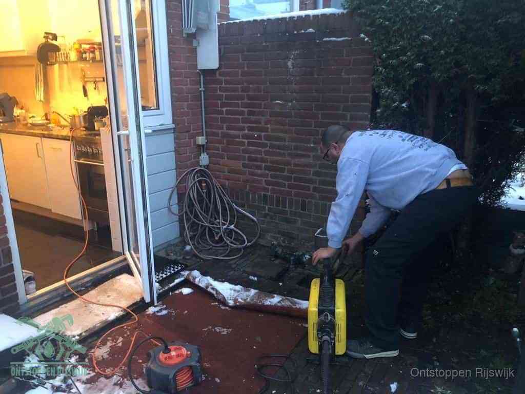 Een monteur werkt buiten bij een open riool-/grondput met een elektrische ontstoppingsmachine om een verborgen afvoerprobleem op te sporen in Rijswijk
