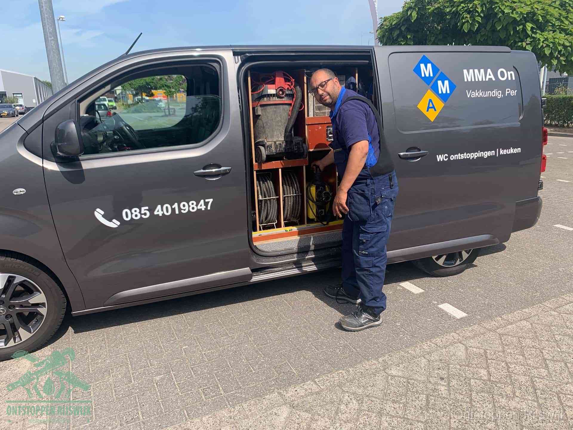 Een monteur bij de open schuifdeur van zijn bedrijfsbus op een parkeerplaats, klaar om de oorzaak van terugkerende afvoerverstoppingen aan te pakken in Rijswijk