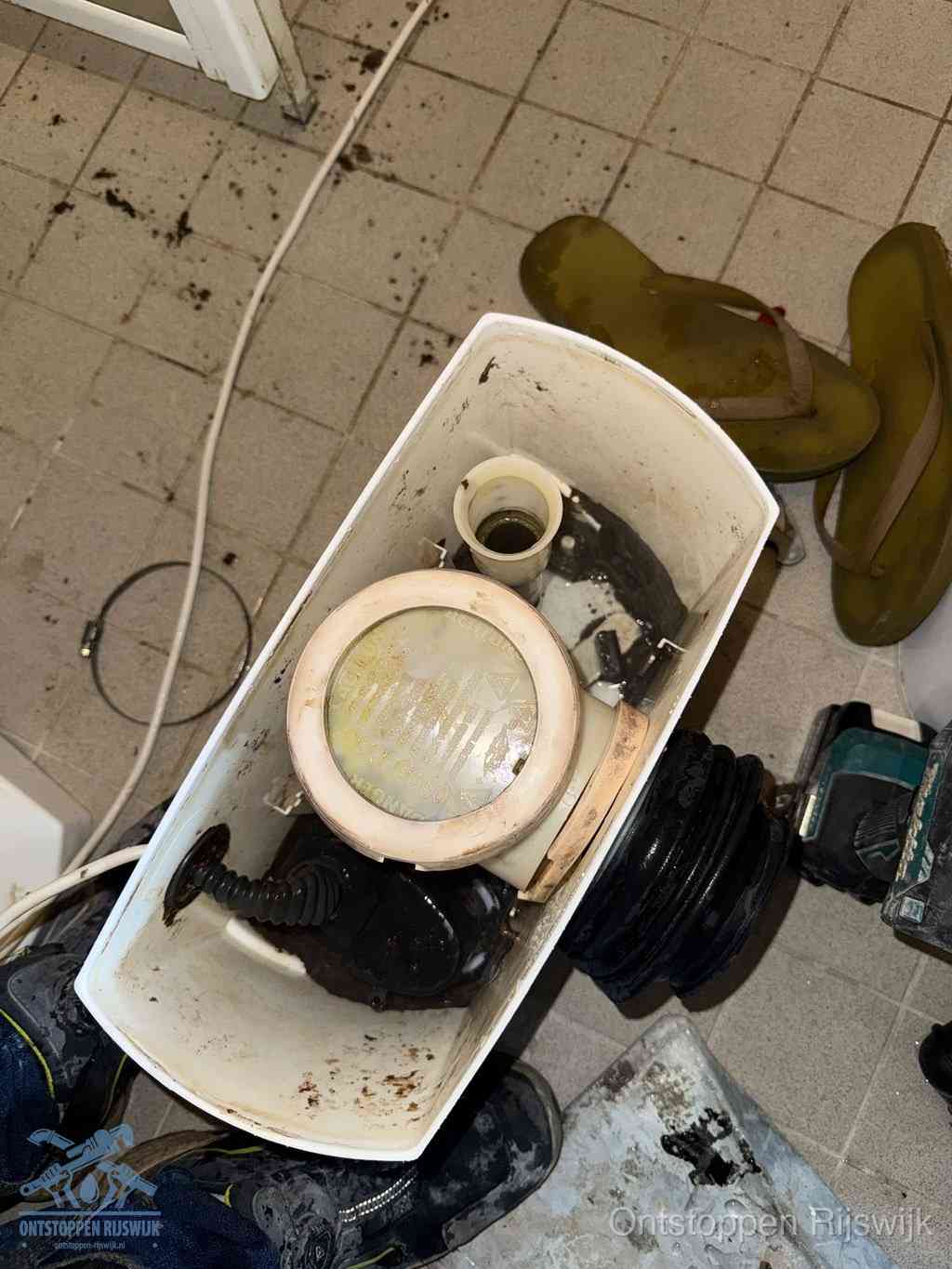 Een gedemonteerde toiletpot op de vloer met ontstoppingsveer en gereedschap ernaast, het verwijderen van een vastzittend voorwerp uit de wc in Rijswijk