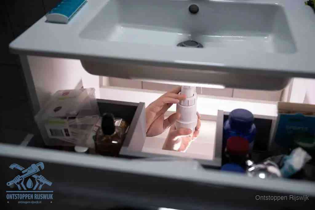 Een pompfles met zeep boven een wastafel in de toiletruimte, de warm water en afwasmiddel-methode om de wc te ontstoppen in Rijswijk