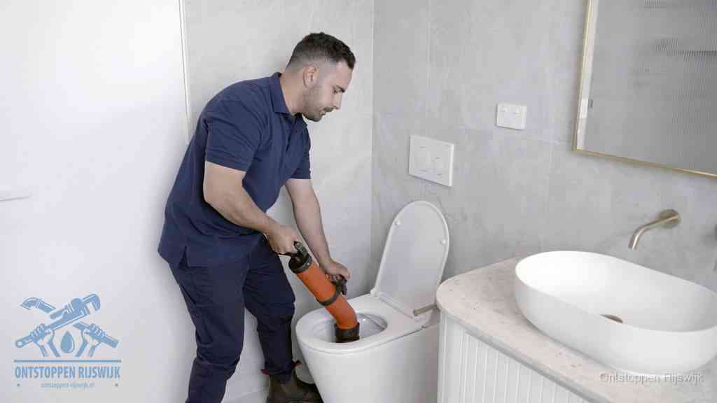 Een man gebruikt een handmatige luchtdruk-ontstopper in een modern betegeld toilet om zelf de wc te ontstoppen in Rijswijk